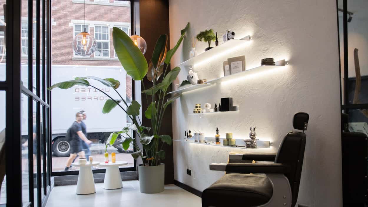Entree met kappersstoel, plant en verlichte schappen met producten